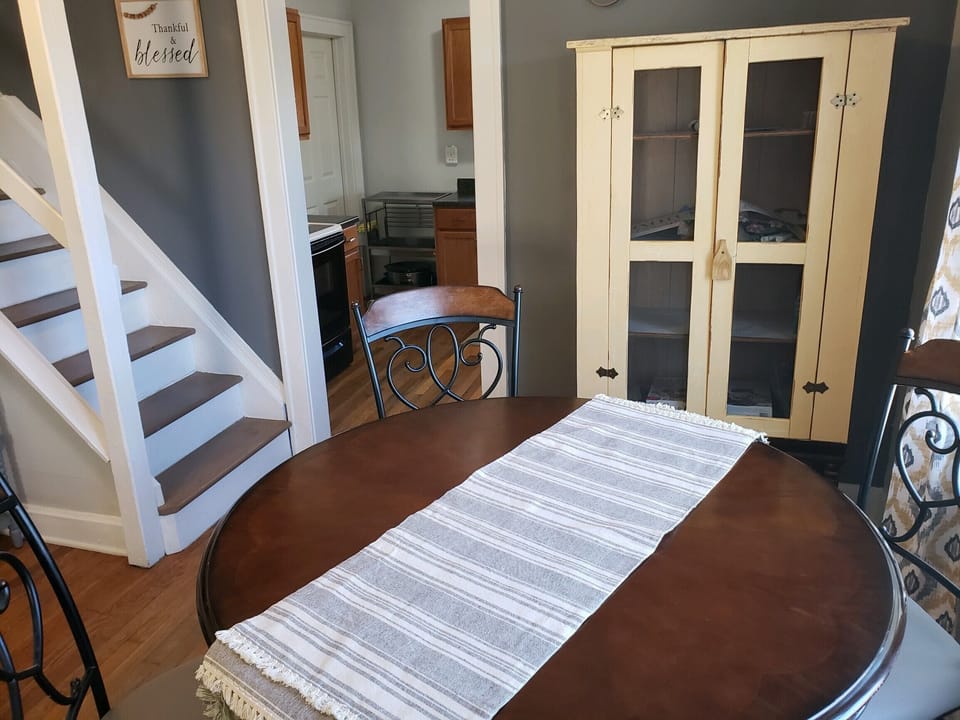 View of round counter height table, vintage cupboard and stairs leading upstairs