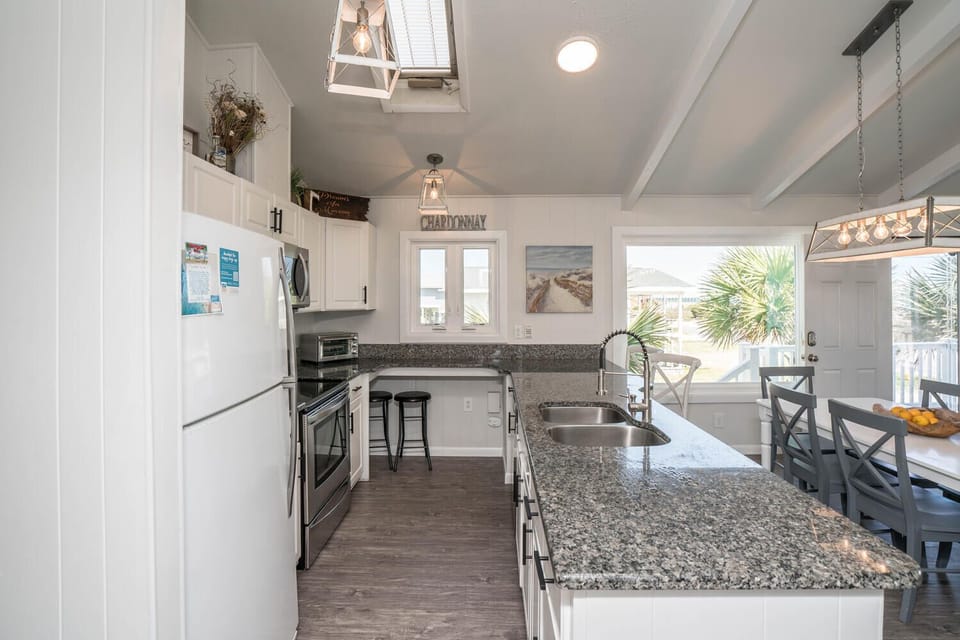 Light-filled coastal kitchen featuring granite countertops, white cabinetry, stainless steel appliances, skylight, and a spacious breakfast bar—ideal for cooking, casual dining, and gathering with family and friends.
