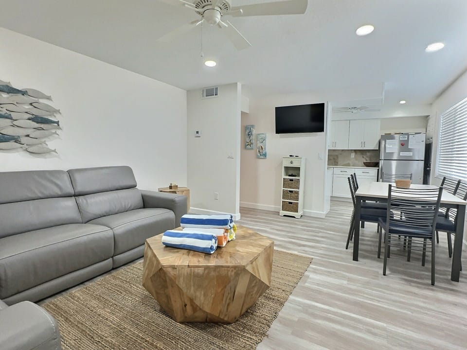 Open-plan living room with sofa, coffee table, dining area, and mounted TV