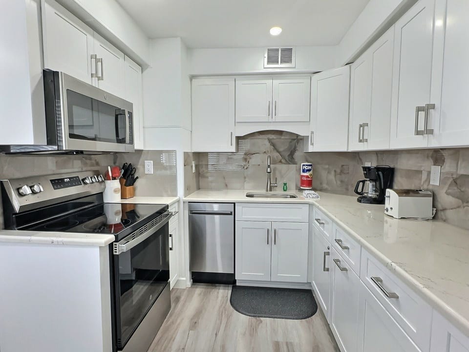 Updated kitchen with white cabinets, stainless appliances, and tile backsplash