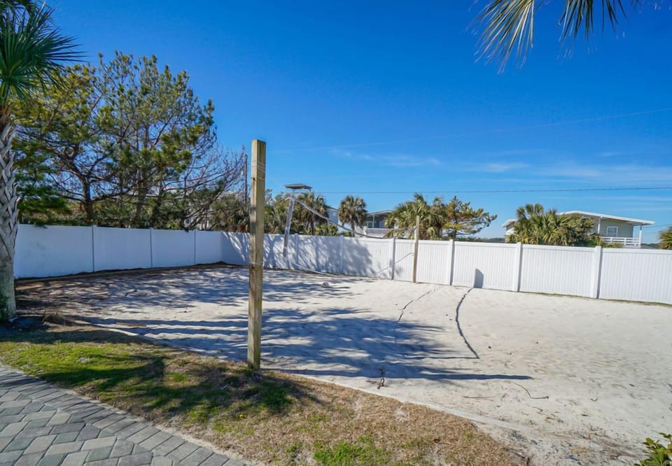 Private volleyball court surrounded by tropical palms and white fencing offers endless entertainment under blue skies.