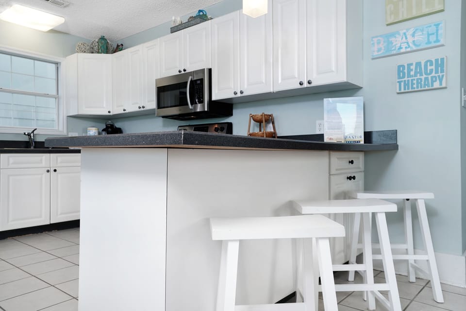 Your bright, beachy kitchen invites morning coffee at the breakfast bar while coastal artwork sets a relaxing vacation mood.