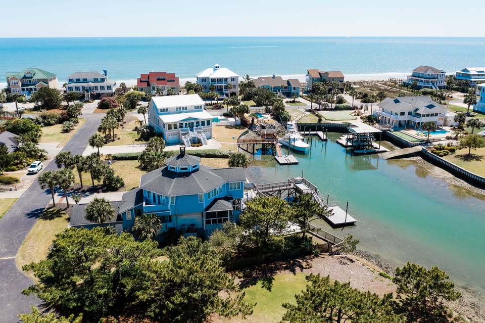 Aerial view of waterfront vacation homes nestled along pristine coastline with private docks and crystal-clear turquoise waters nearby.