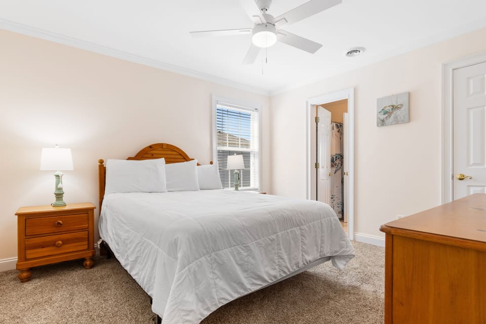 Sink into crisp white linens and warm wood furnishings in your peaceful bedroom retreat, complete with ceiling fan for ultimate comfort.