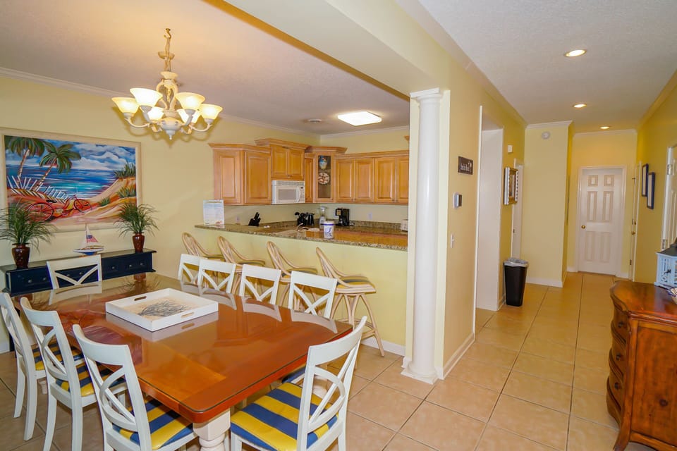 Your bright open-concept living space flows seamlessly from dining to kitchen, with tropical artwork and warm yellow walls creating a sunny, welcoming atmosphere.