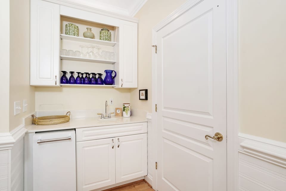Your private butler's pantry makes entertaining effortless, with crisp white cabinetry, gleaming counters, and charming blue glassware ready for your gatherings.