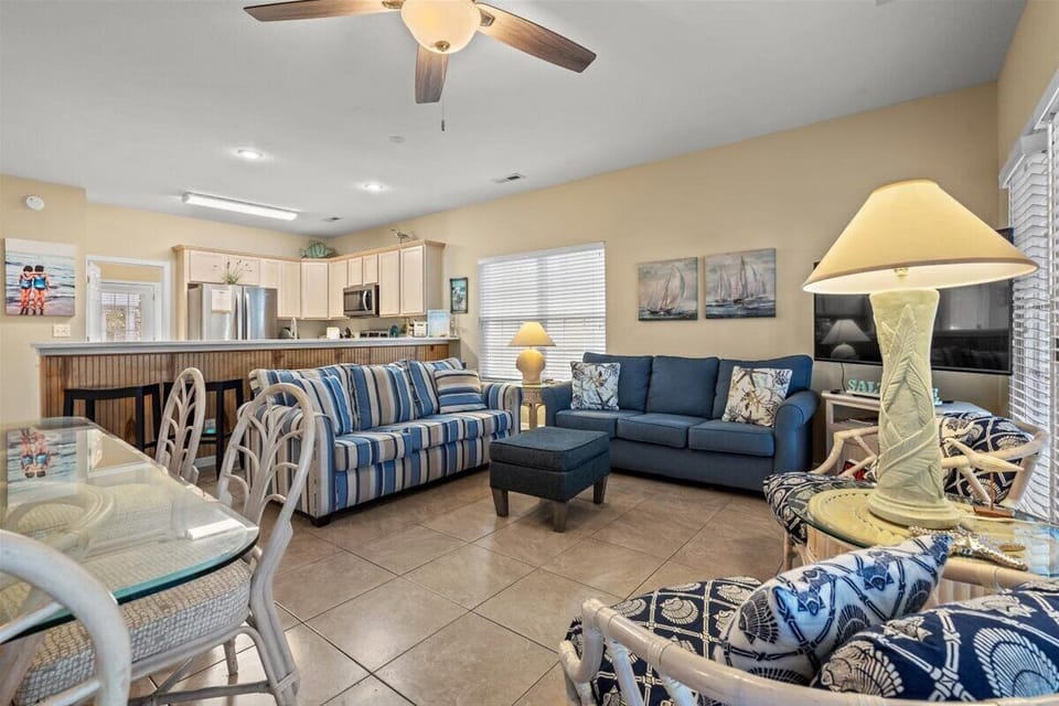 Relax in your spacious living area featuring coastal blues, comfy seating, and an open kitchen—perfect for gathering with loved ones.
