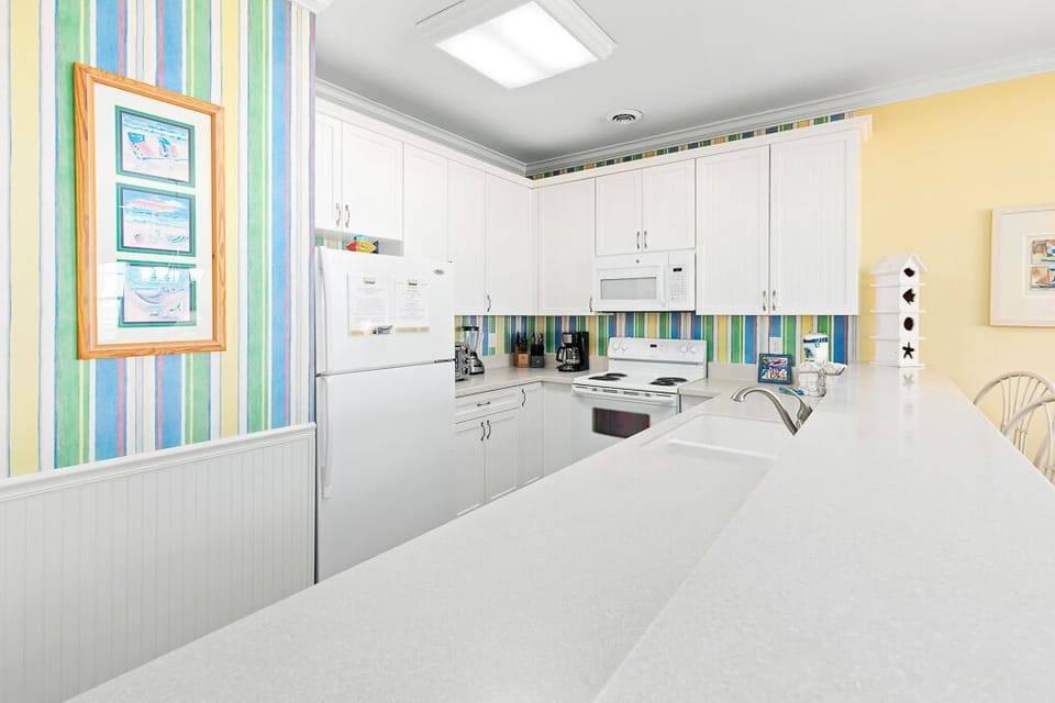 Your bright, fully-equipped kitchen awaits with cheerful striped accents, white appliances, and plenty of counter space for preparing memorable meals.