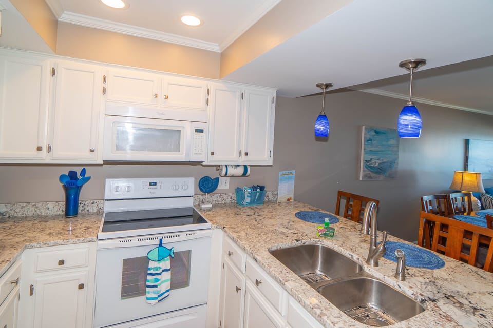 Your fully equipped kitchen features granite counters, white appliances, and cheerful blue accents for memorable meal prep during your stay.