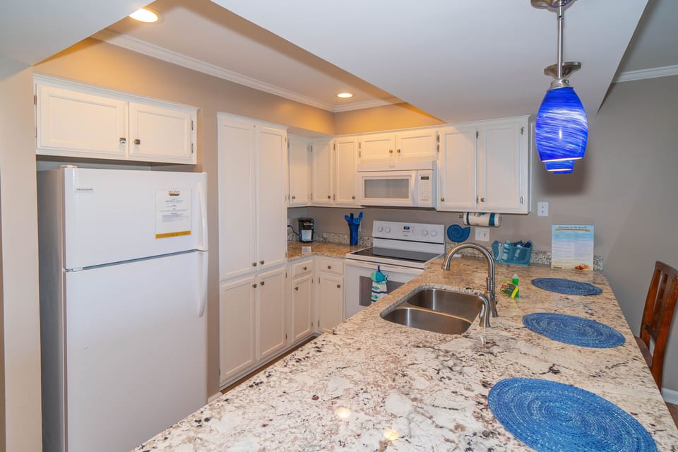 Your fully equipped kitchen features granite countertops, white cabinetry, and modern appliances, perfect for preparing meals with stunning blue accents throughout.