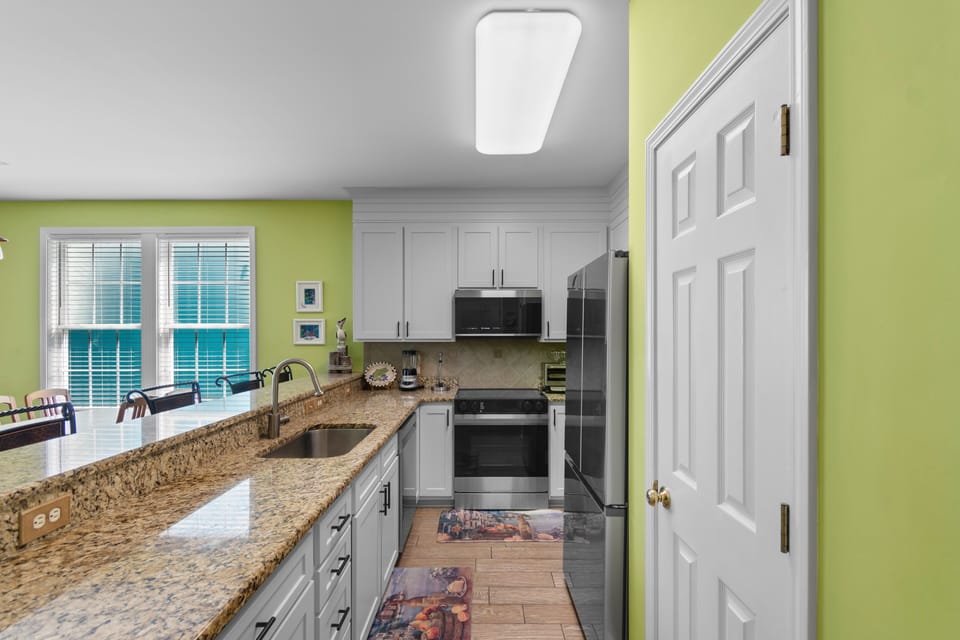 Your bright, fully-equipped kitchen awaits with granite countertops, stainless steel appliances, and cheerful green walls that make cooking feel like pure joy.