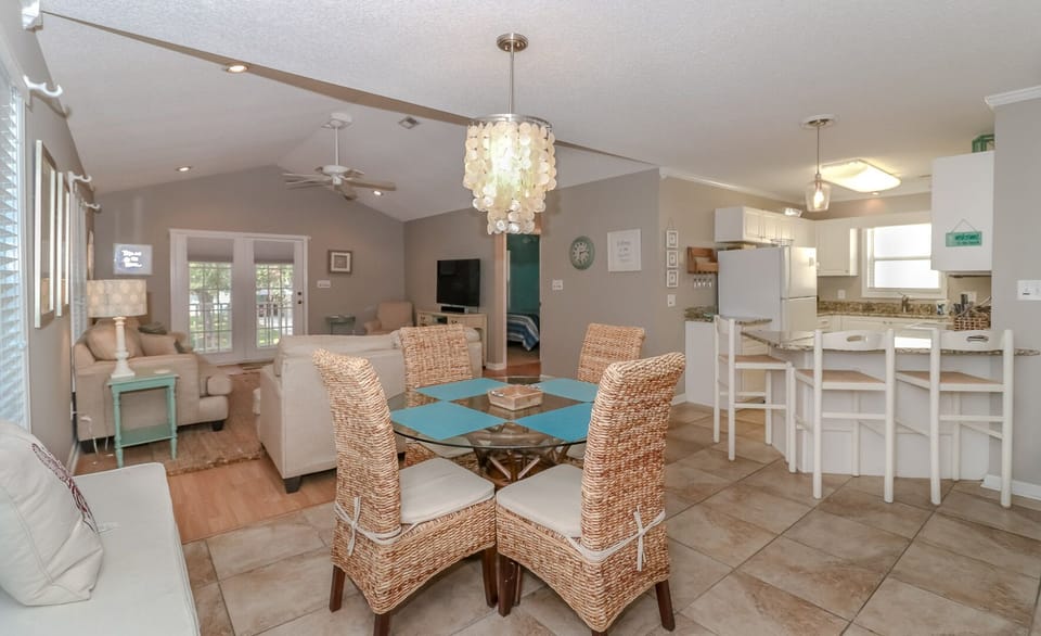 Your open-concept haven seamlessly blends dining and living spaces, where coastal charm meets modern comfort under elegant pendant lighting.