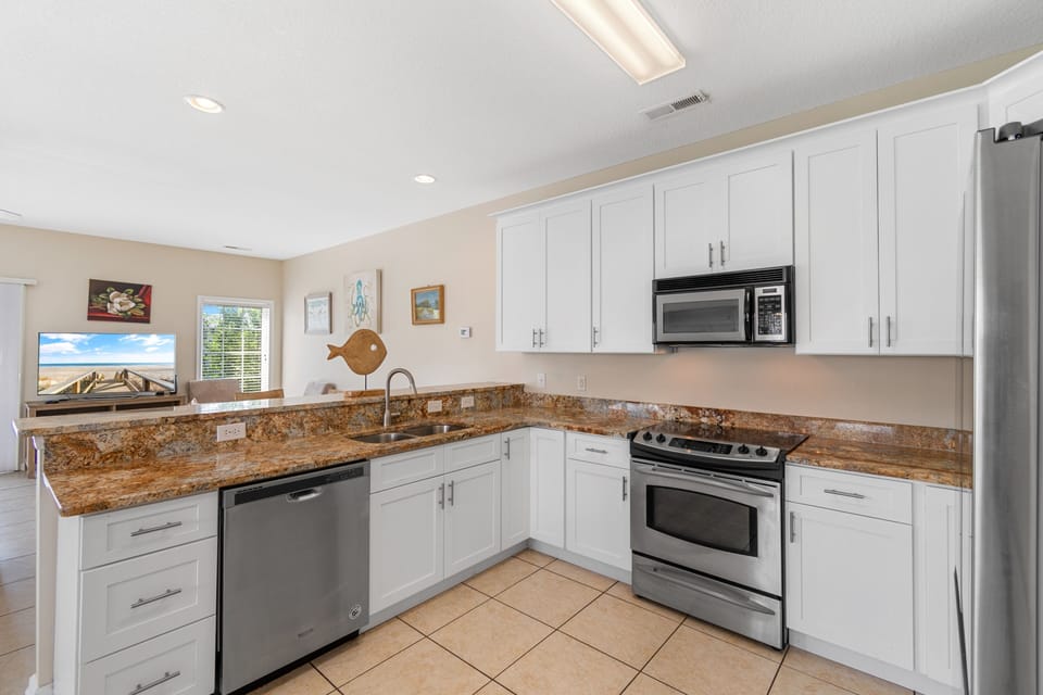 Your fully equipped kitchen features granite counters, stainless steel appliances, and bright white cabinets perfect for preparing vacation meals together.