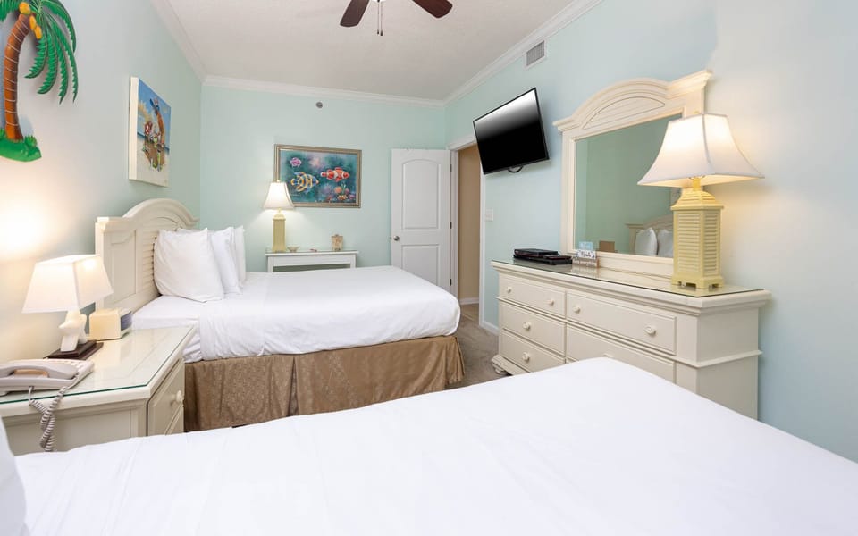 Bright guest bedroom featuring two double beds, a wall-mounted TV, and coastal artwork, creating a cheerful atmosphere