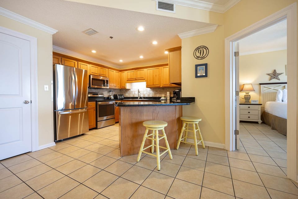 Modern kitchen features wooden cabinetry, granite countertops, and a breakfast bar with yellow stools