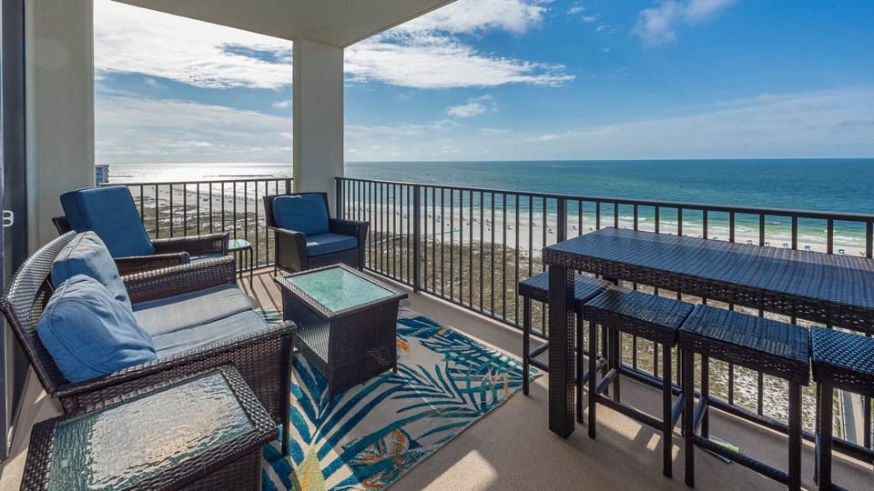 Cozy balcony features comfortable seating and a high-top table, offering sweeping views of the tranquil gulf and beach below