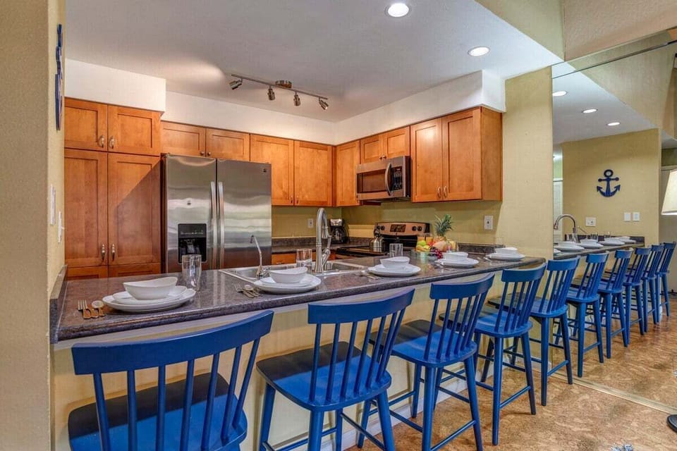 Kitchen and dining area with a long breakfast counter, bold blue seating, and warm wood cabinetry.