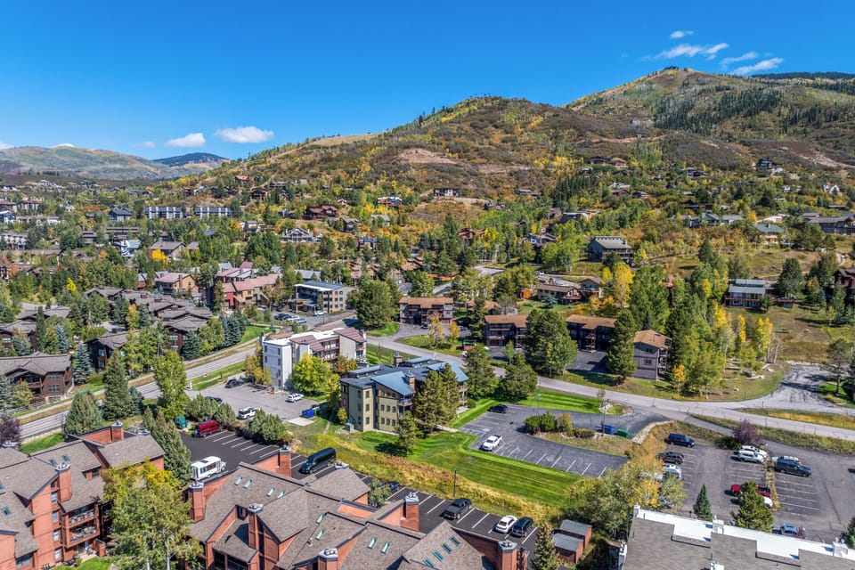 Aerial view of a mountain resort neighborhood with residential buildings nestled among fall foliage and alpine terrain, showcasing the scenic hillside setting and surrounding natural landscape.