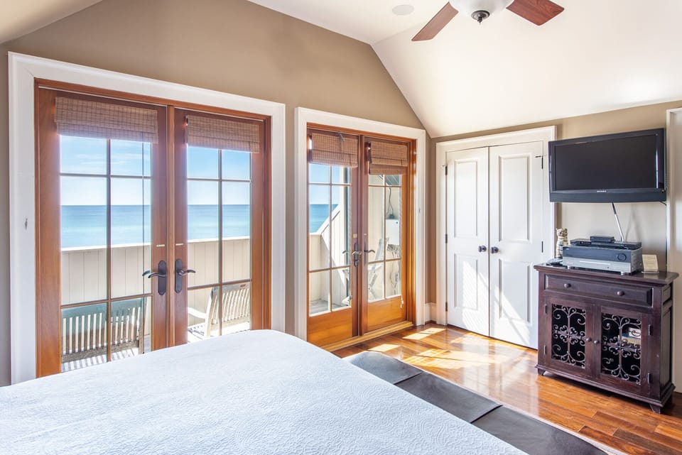 Window Doors to the Balcony, Large Bed, TV, Ceiling Fan, and Buffet Console.