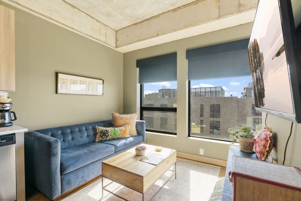 Relax in your stylish living room with exposed beam ceilings, plush velvet seating, and city views through large windows.