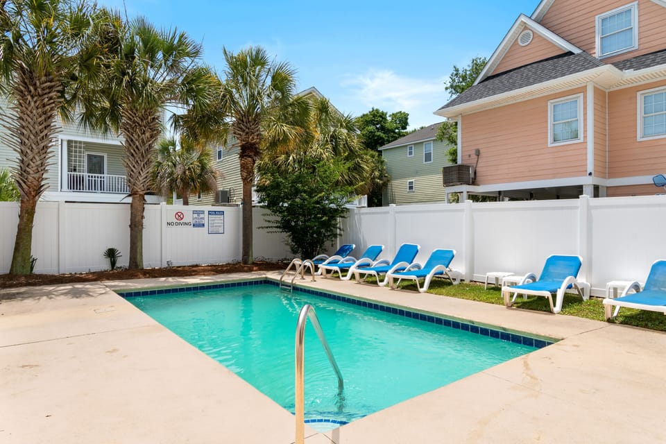 Dive into your private oasis! This sparkling pool beckons you to cool off while lounging on comfortable chairs under swaying palms.