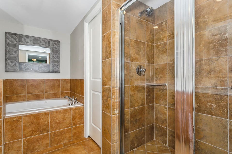 Sink into your own spa-like bathroom retreat, featuring a gleaming glass-enclosed walk-in shower and deep soaking tub framed in warm amber tiles. Your personal sanctuary awaits.