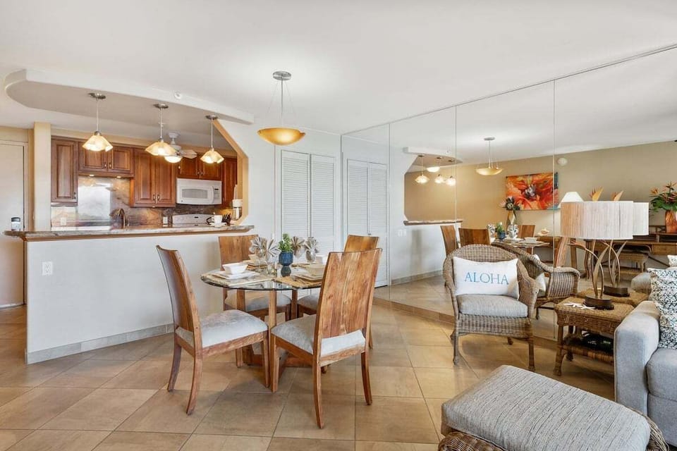 Dining area with a view into the kitchen featuring wooden cabinetry, pendant lighting, and a mirrored wall that enhances the sense of space.