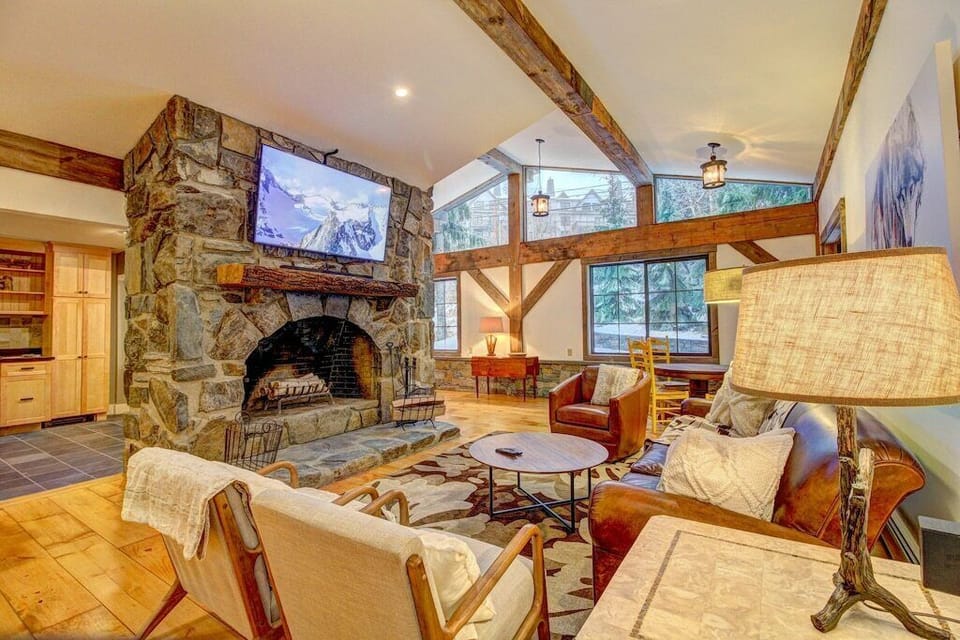 - Rustic living room with a grand stone fireplace and mountain lodge charm   - Cozy seating, wood beams, and large windows for natural light   - Perfect for relaxing after skiing or mountain adventures