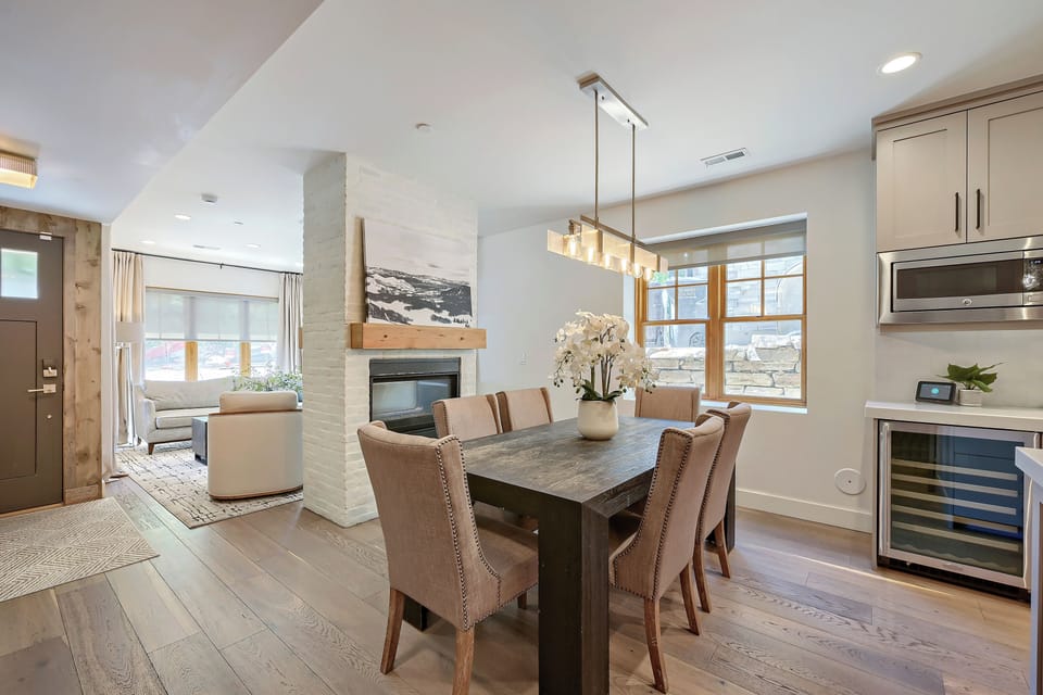 Gather around this elegant dining table where you'll share meals beneath a modern chandelier, with mountain views framing your moments and a cozy fireplace nearby for warmth.