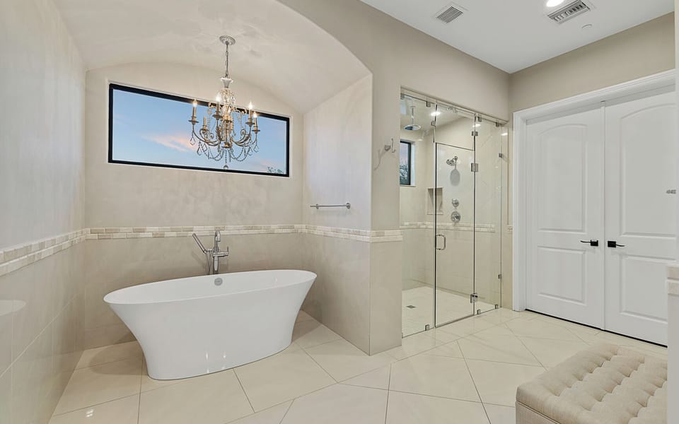 Primary bath with soaking tub, chandelier, glass shower, and natural light