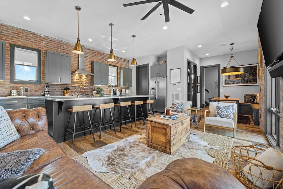 Bright and stylish living area featuring exposed brick walls, large windows with plenty of natural light, comfortable seating, a Smart TV, and a cozy modern-industrial design.
