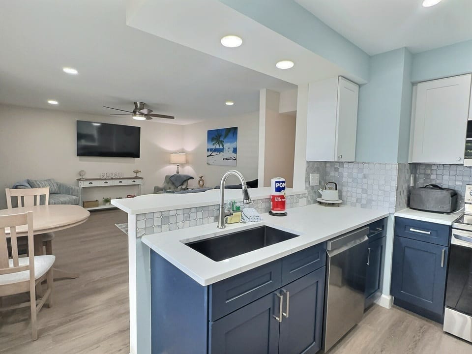 Open kitchen with large island, cooktop, and open view to living area with TV