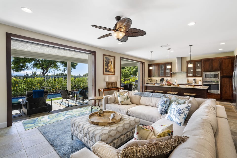 The spacious great room of this Kona Hawai'i vacation rental with a large sectional couch and doors to the back lanai open.