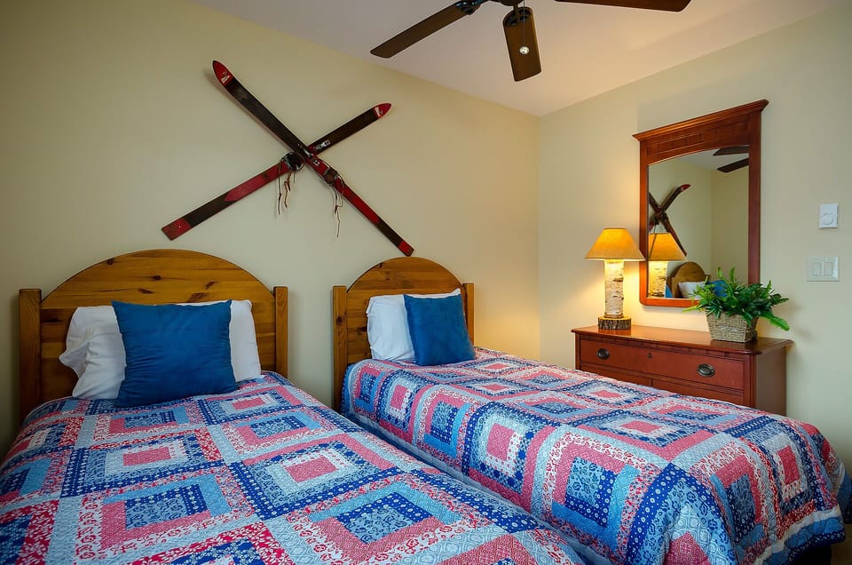Cozy up in this charming twin bedroom featuring handcrafted quilts and rustic ski decor that creates your perfect mountain retreat atmosphere.