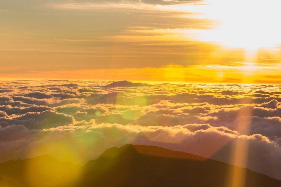 A breathtaking sunrise above the clouds, casting golden light across mountain peaks and a sea of mist.