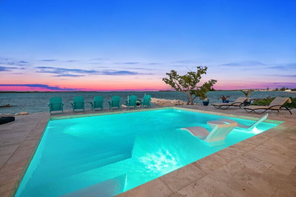 An illuminated waterfront pool beneath a pink and purple evening sky.