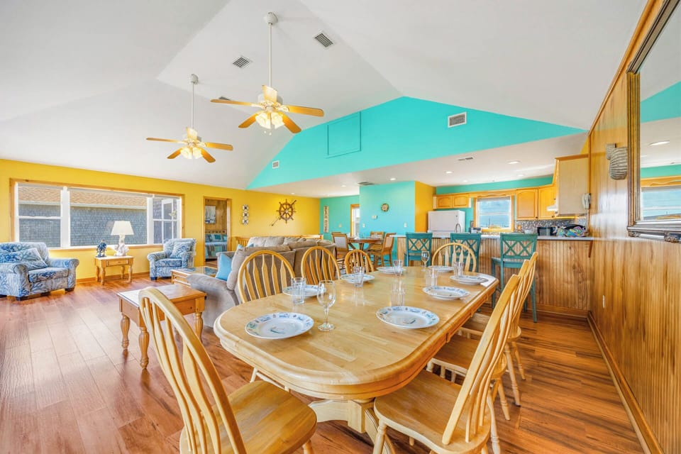 Gather at the spacious dining table where cheerful coastal colors meet warm wood tones, creating the perfect setting for shared meals and laughter with your group.