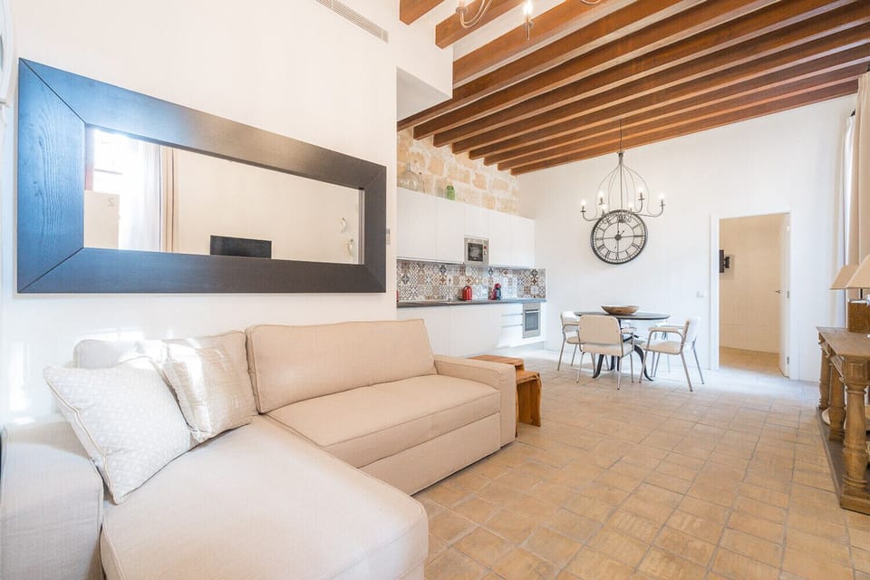 Vintage Palma palace, apartment 2, ground floor is a vacation rental apartment for 2 adults and 2 children in Palma de Mallorca. You can see almost the entire apartment here, with the sofa bed in the foreground and the kitchen with oven, hob and dishwasher to the left. The bathroom is to the left after the sofa. At the end you have the bedroom. Natural light comes from a window on the right.