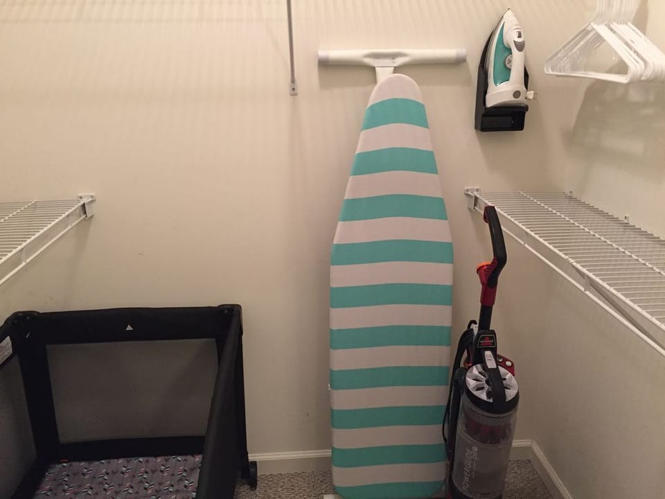 3rd floor primary closet with iron board, vacuum, and pack & play