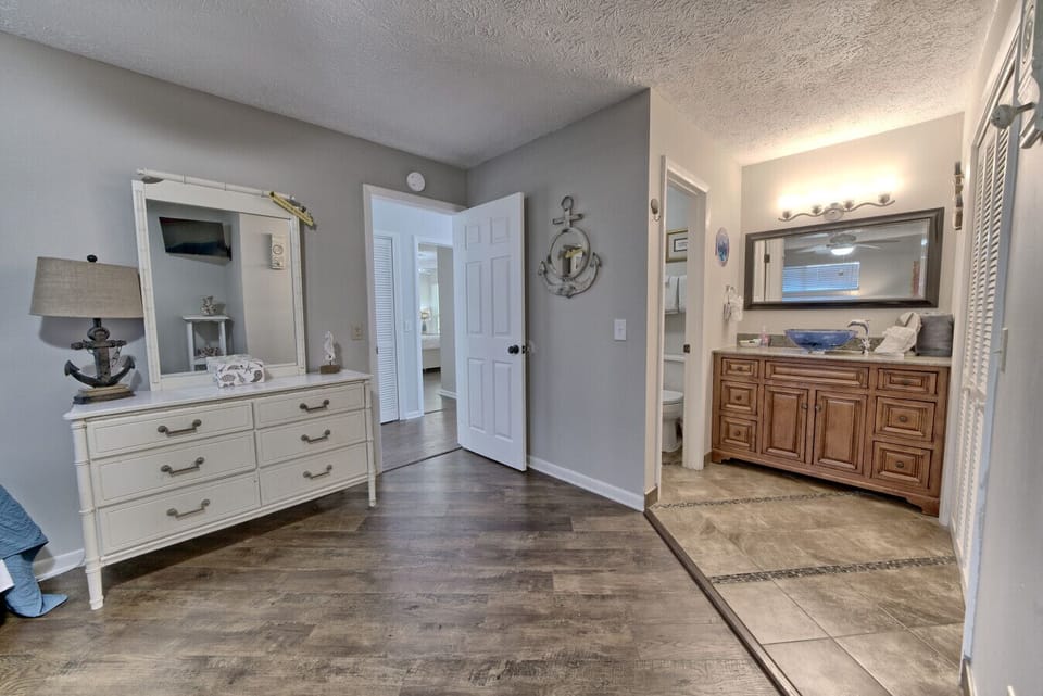 This thoughtfully designed space blends a coastal vibe with modern convenience, featuring a stylish dresser and an en-suite vanity for a touch of luxury.