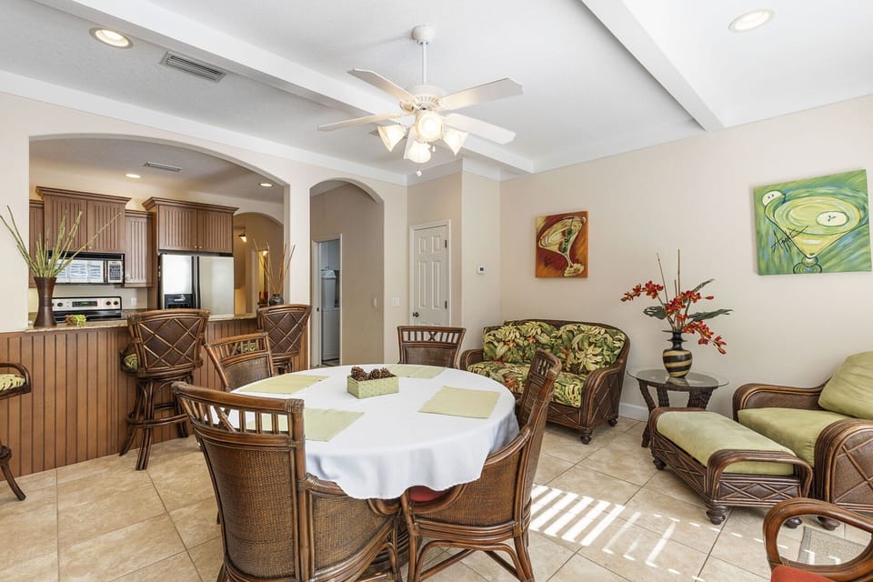 Dining room with round table, wicker furniture with tropical cushions, and arched entryway to kitchen