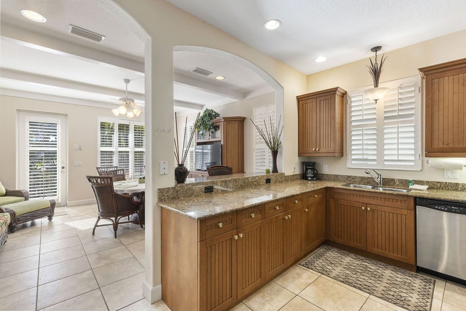 Kitchen with wood cabinets, granite countertops, dishwasher, and open view to dining area through archway