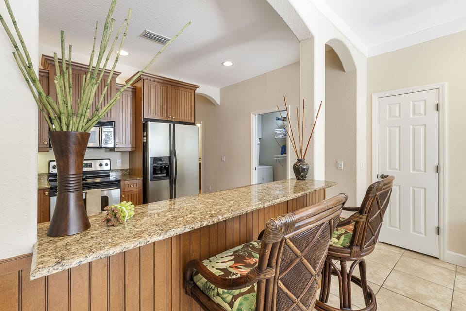 Kitchen with granite-topped island and bar stool seating, stainless steel refrigerator, and wood cabinets