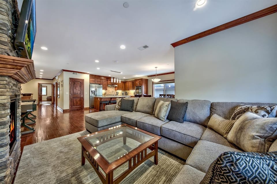 Relax in your spacious living room featuring plush sectional seating, stone fireplace, and open-concept kitchen perfect for entertaining.