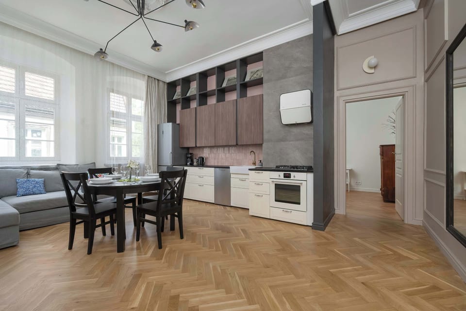 A kitchen and dining area with white cabinetry, wooden flooring, and plenty of natural light from the tall windows.