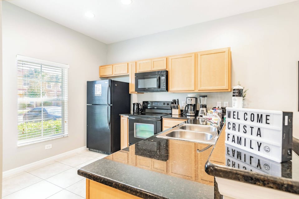 Step into this cheerful kitchen, where warm wood cabinetry complements sleek black appliances. Sunlight streams through the window, illuminating the polished countertops and inviting you to whip up a delightful meal.