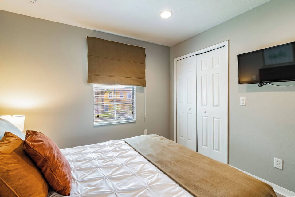 Experience a cozy bedroom with a plush queen bed dressed in warm, earthy tones and inviting pillows. Natural light flows in, accentuating the modern decor and a wall-mounted TV for your convenience.