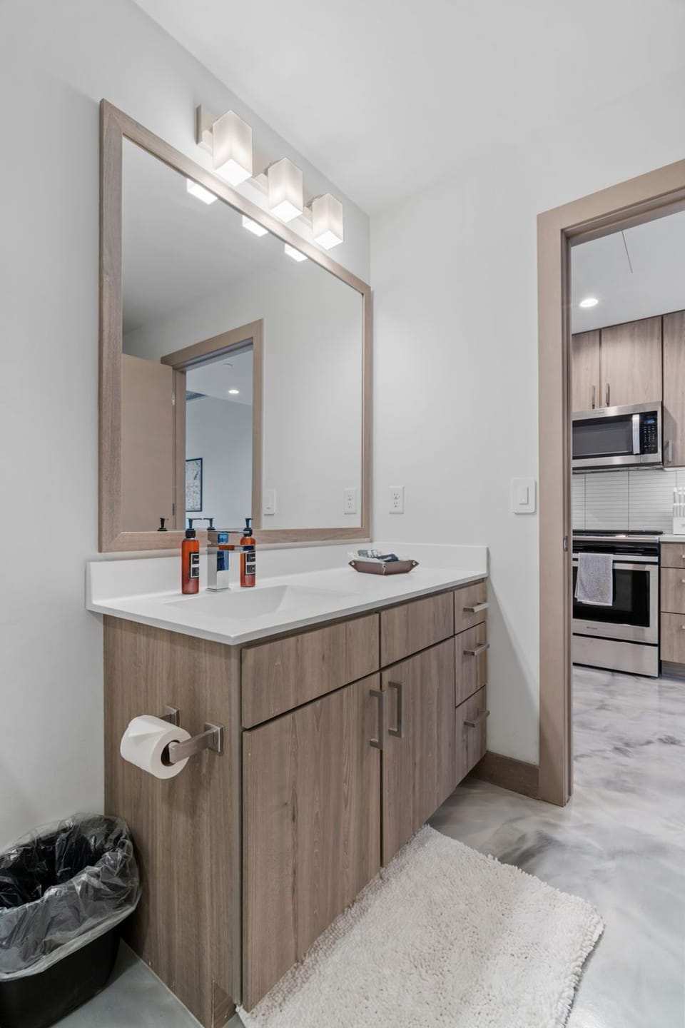 Your modern bathroom features warm wood vanity, bright lighting, and seamless access to the fully equipped kitchen.