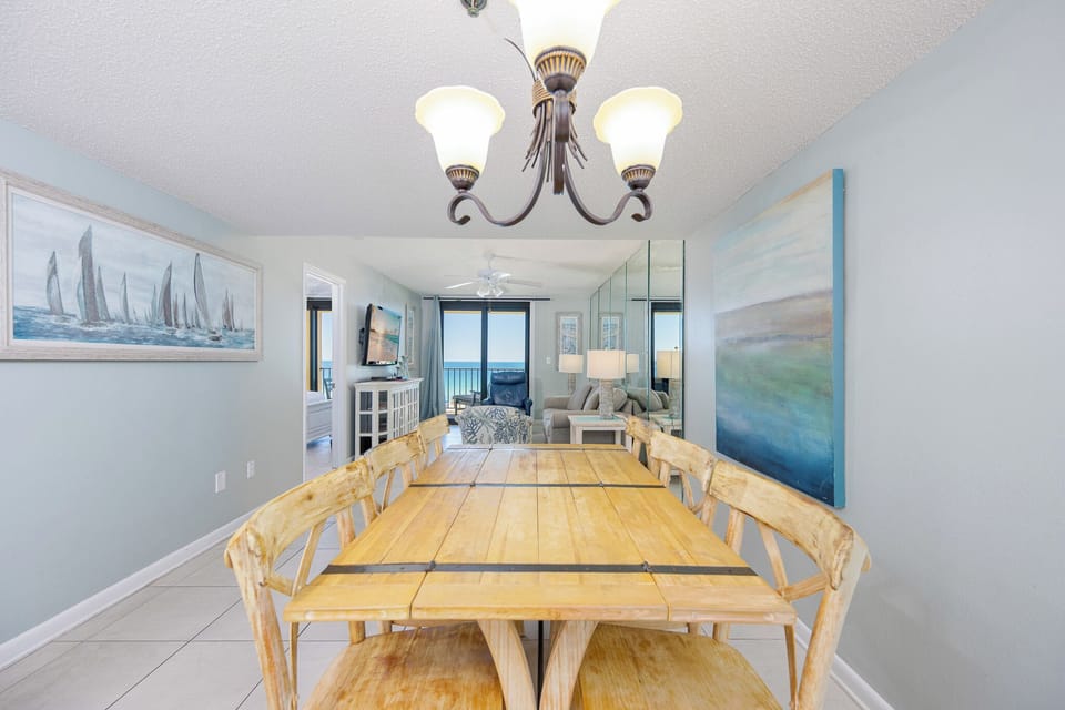 This dining area features a rustic table with six chairs, complemented by a stylish chandelier and a serene coastal painting