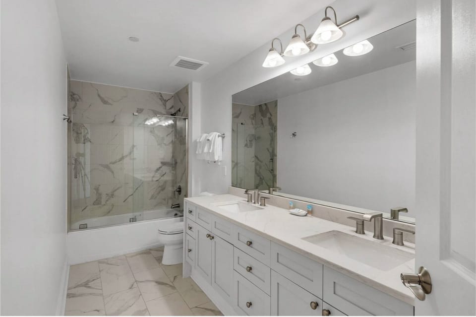 Step into your elegant marble-accented bathroom with dual vanities, brilliant lighting, and a luxurious glass-enclosed shower waiting for your relaxation.